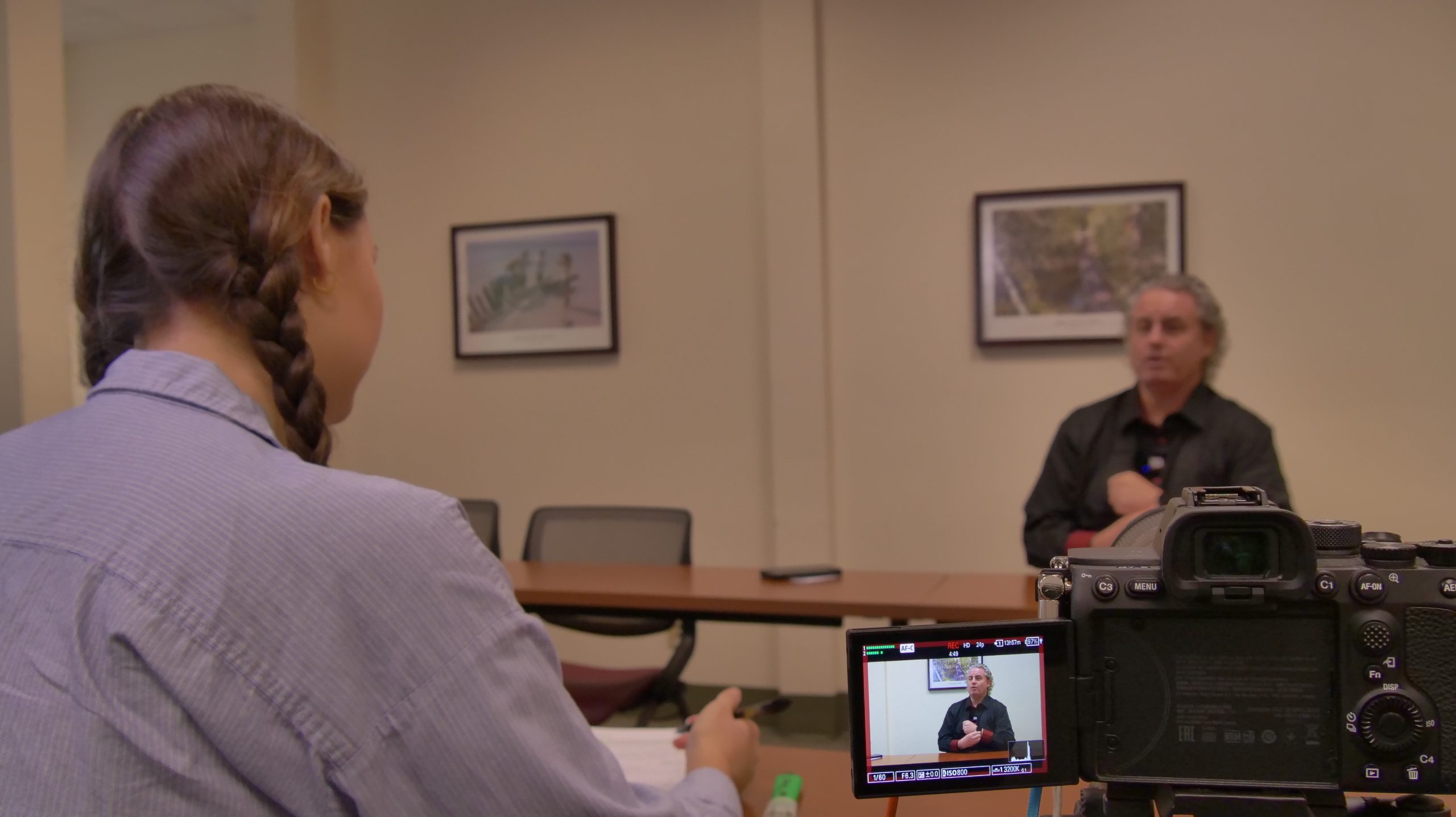 A photo depicting SPOHP intern Mattison Mathews interviewing narrator Michael Dawson inside of a sparsely decorated beige classroom.